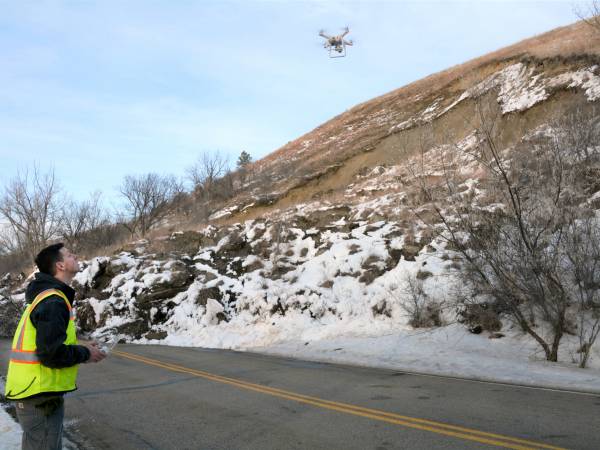 A color photograph of a man operating a drone over a landslide.