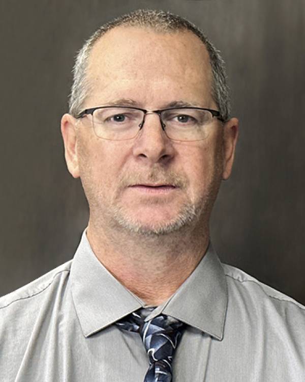 Headshot of Kent Hollands wearing a gray shirt and black tie.