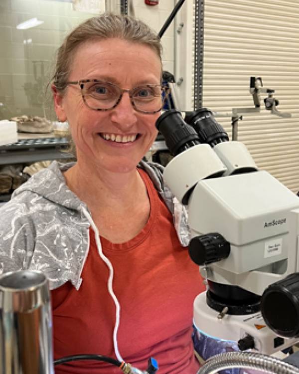 Cathy Lash wearing a dark orange shirt posing by a microscope in the lab.