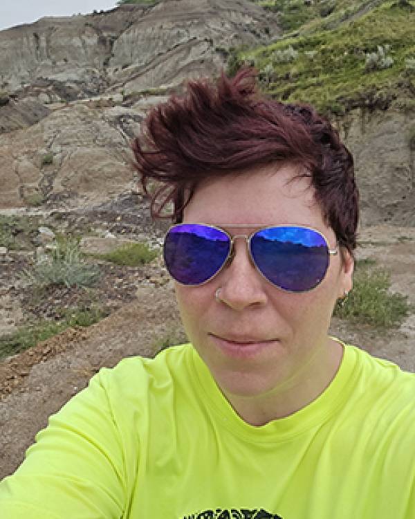 Selfie of Alex Gardner standing outdoors wearing a bright yellow shirt and sunglasses.