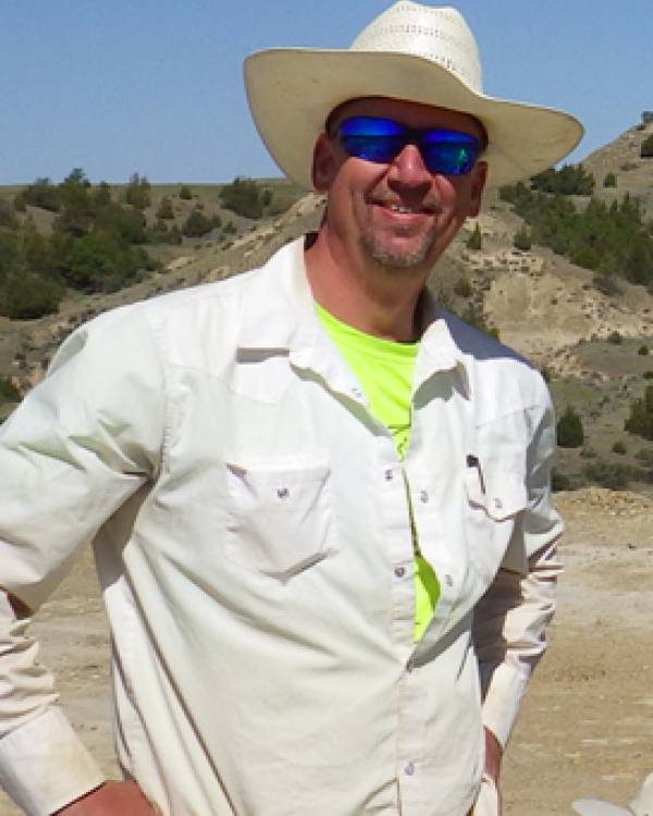 Jeff Person standing outdoors wearing a long-sleeved white shirt and cowboy hat.
