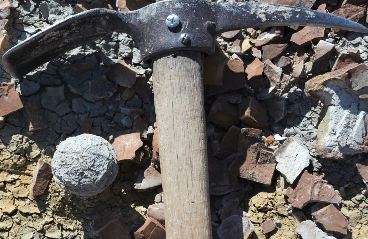 A pick axe laying in rocks next to a round, gray nodule.
