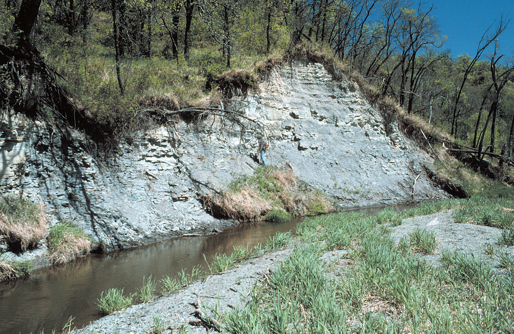 A man standing on a gray bank beside a river.