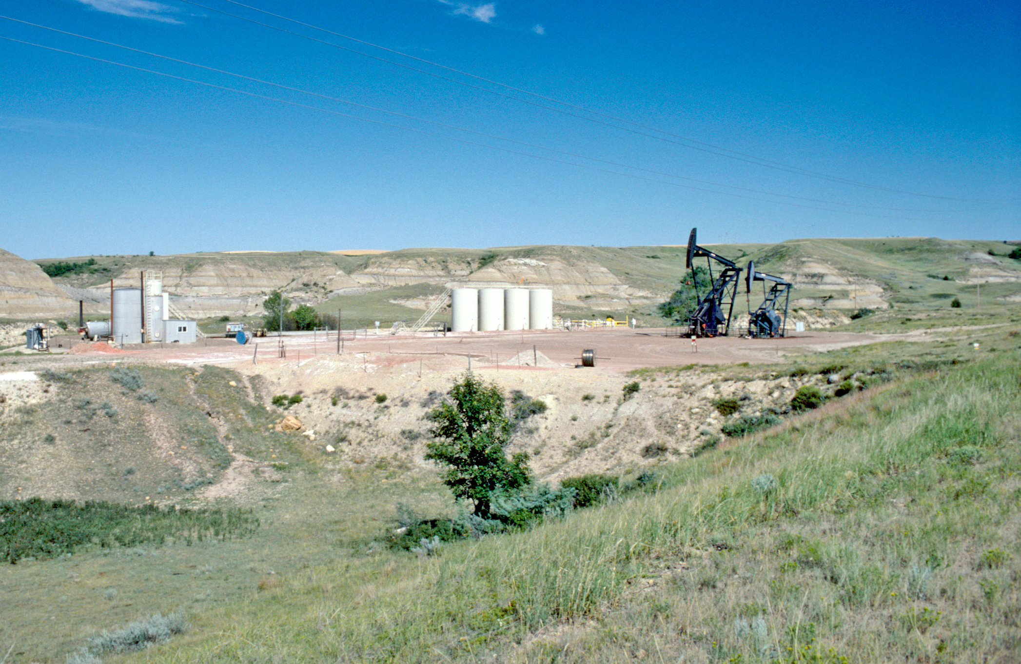 Two oil pumpers near four white tanks.