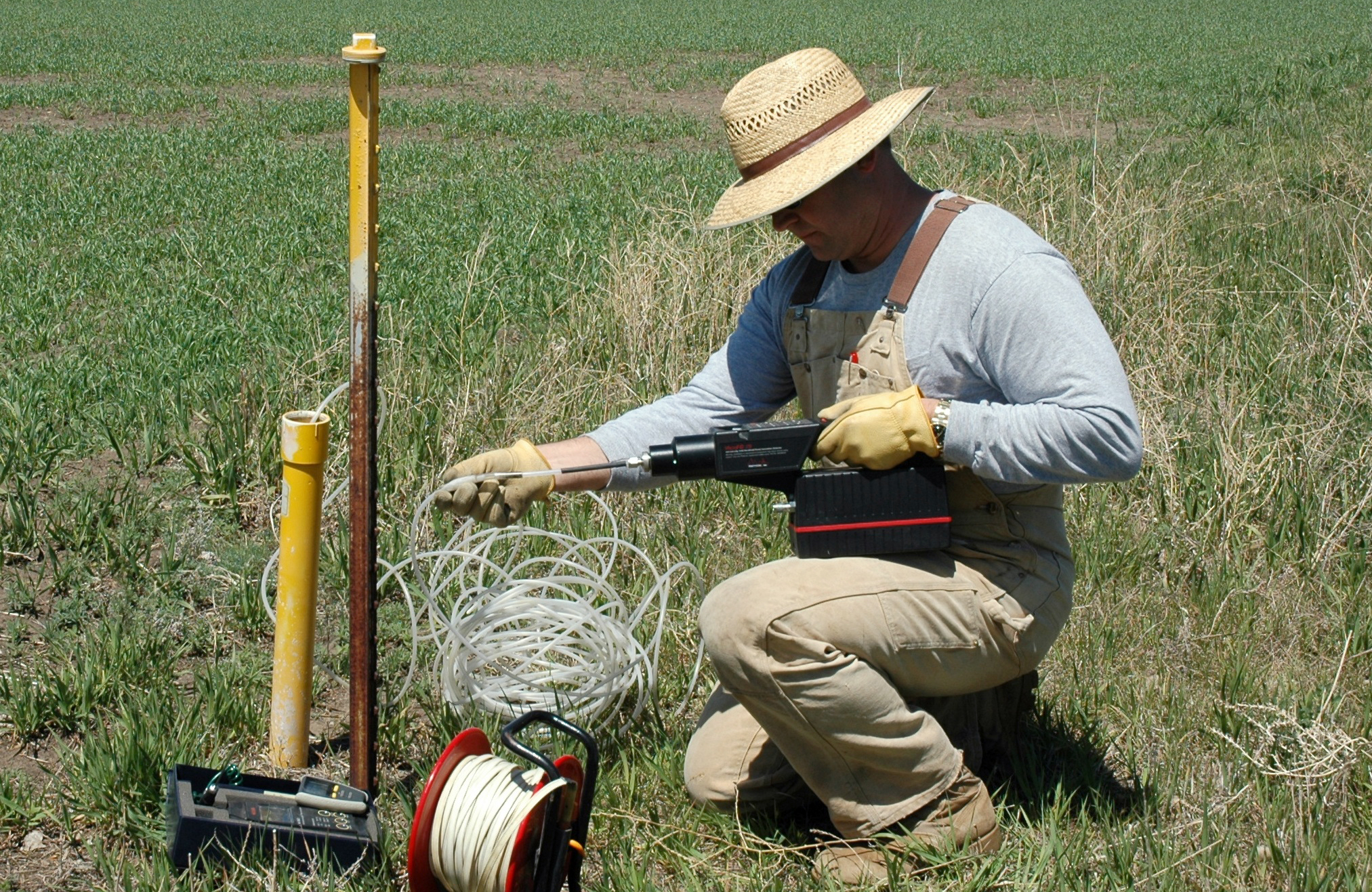 A man using electrical instruments, holding tubing while kneeling in the grass..