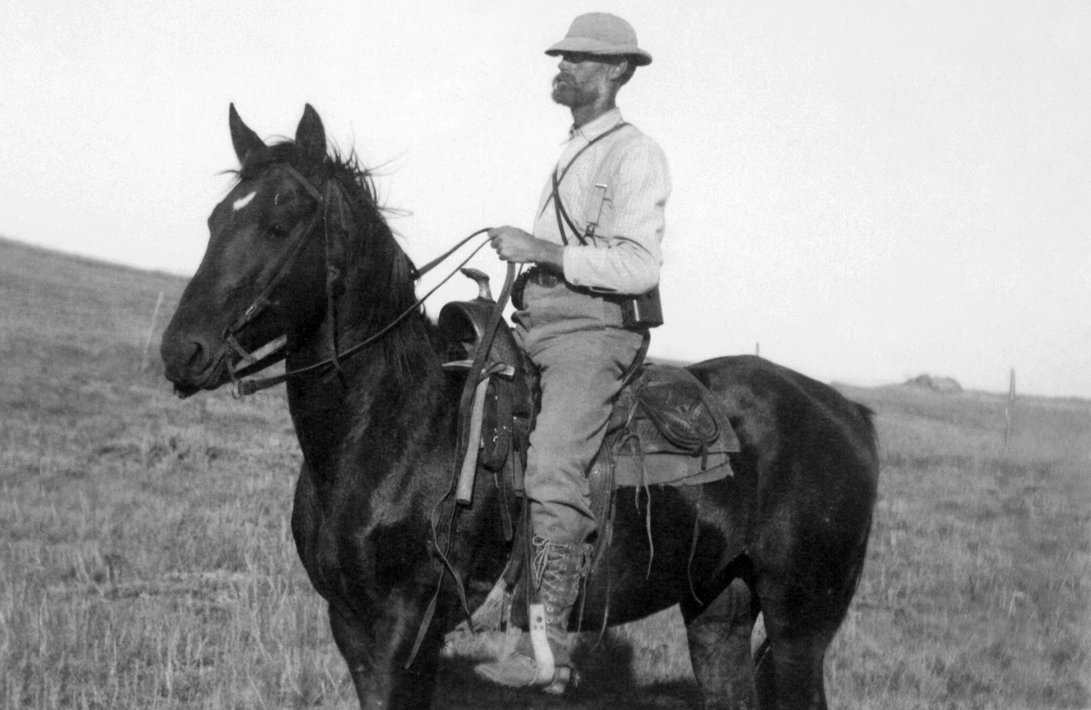 A black and white photo of a man riding a horse.
