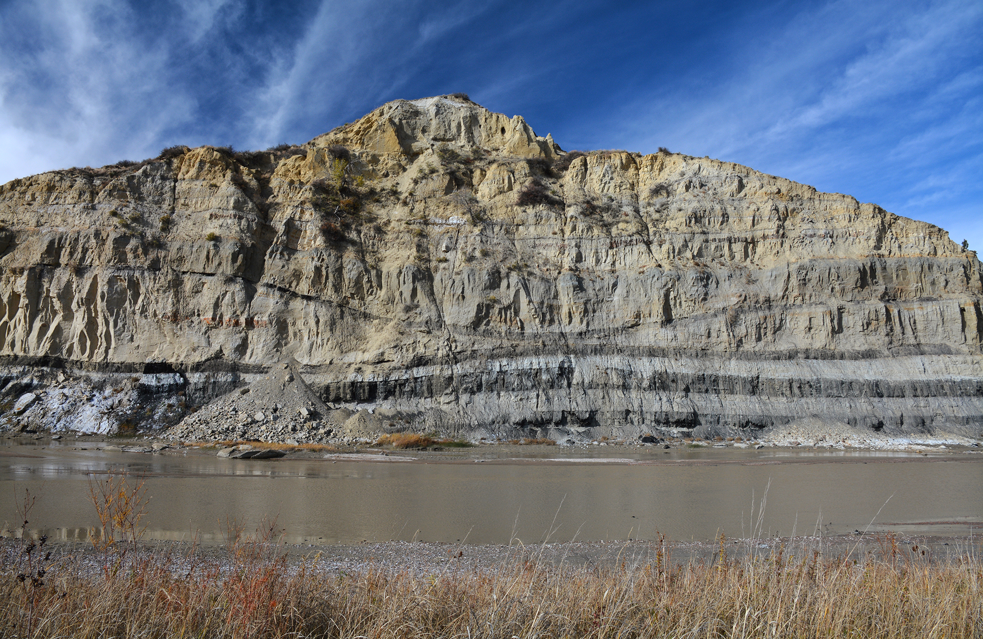 A tall rock formation streaked with coal next to a river against a very dark blue sky.