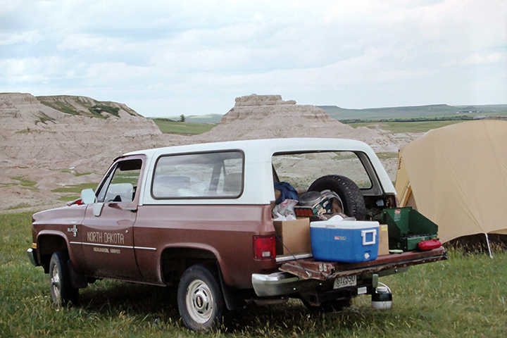 Old vehicle full of supplies parked beside a tent.