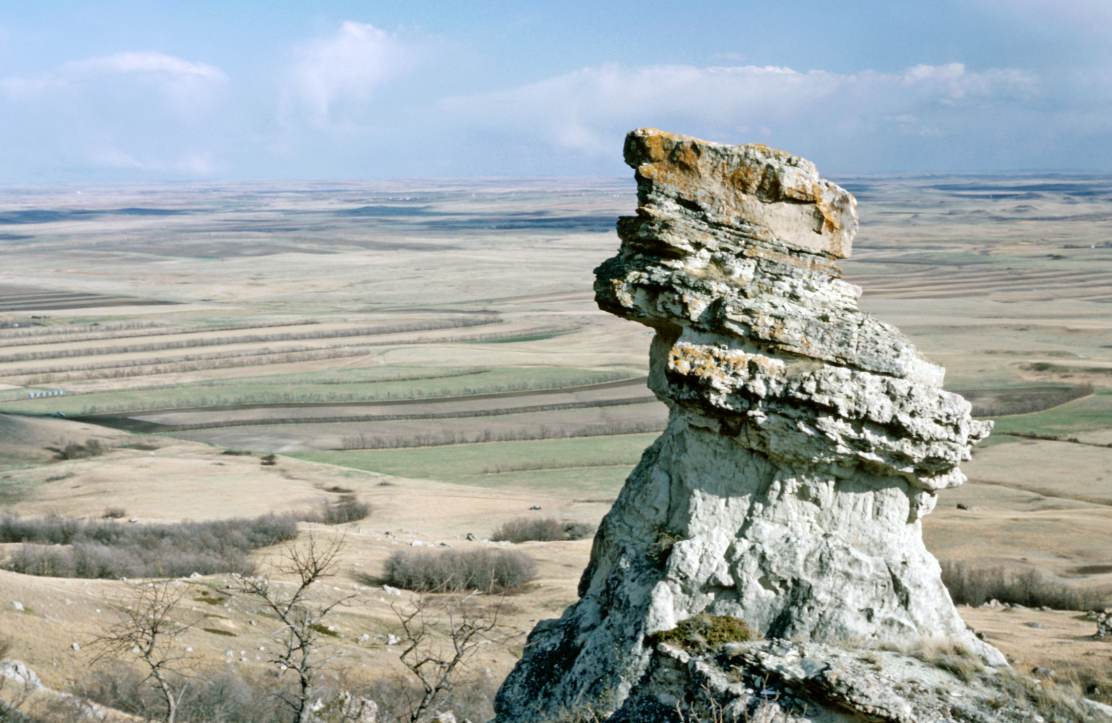 A pedestal rock formation on a hill above fields.