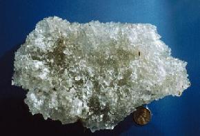 Crystals of mirabolite from salt crust at the base of North Lake, Divide County. Mirabolite (NaSO4.10H2O) is the hydrated 
								mineral form of sodium sulfate. Mirabolite readily converts to a dehydrated mineral form (thenardite) upon heating. The clear crystals throughout this sample are mirabolite 
								while the white crust on the left side of the sample are thenardite. (Photo by E. Murphy, NDGS). 